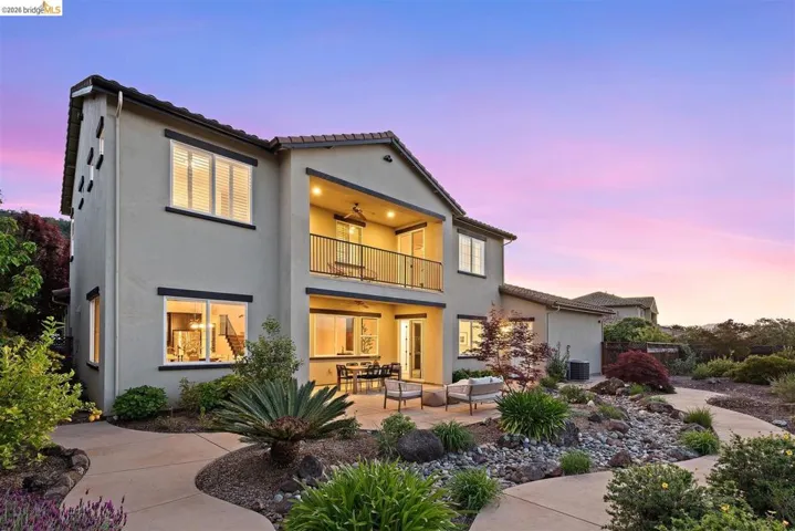 Back of house at dusk featuring a balcony, stucco siding, a patio area, a tile roof, and a ceiling fan