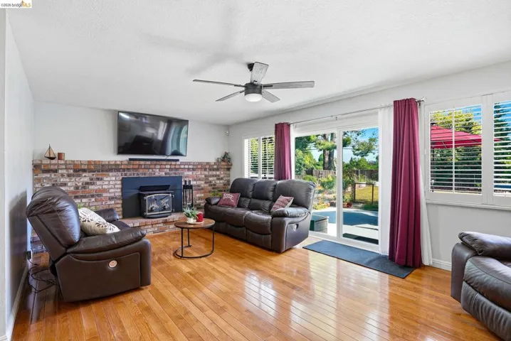 Living area with light wood-type flooring, ceiling fan, a wood stove, and a textured ceiling