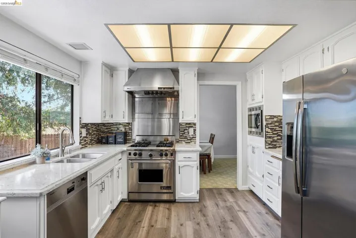 Kitchen with stainless steel appliances, light stone countertops, white cabinets, and exhaust hood
