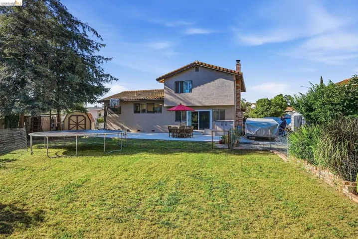 Back of property with a storage unit, a trampoline, stucco siding, a chimney, and a patio area