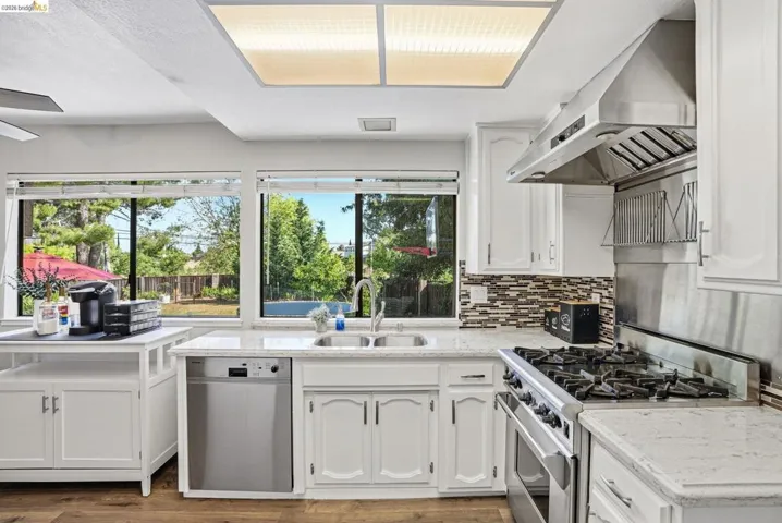 Kitchen featuring stainless steel appliances, white cabinets, ventilation hood, dark wood-style floors, and light stone countertops