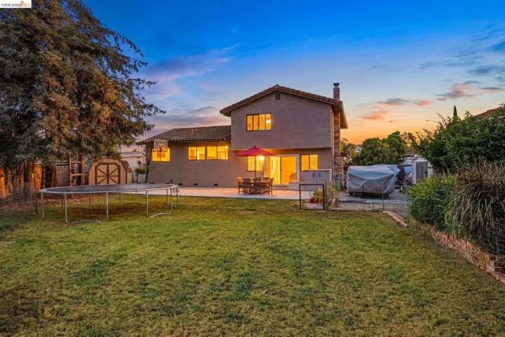 Rear view of house featuring a storage shed, a chimney, a patio, a trampoline, and stucco siding