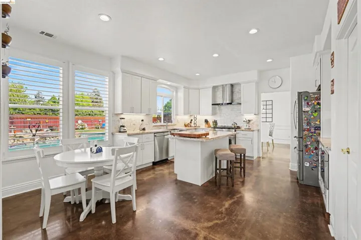 Kitchen with decorative backsplash, a kitchen island, a kitchen bar, finished concrete floors, and light stone countertops
