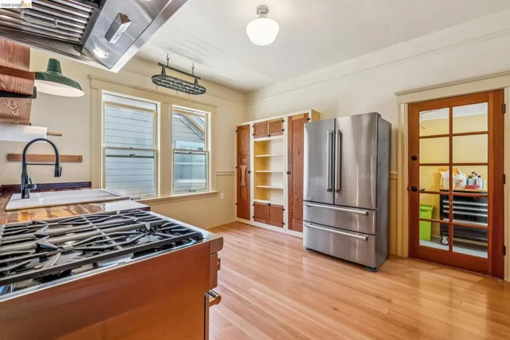 Kitchen featuring freestanding refrigerator, exhaust hood, gas stovetop, light wood finished floors, and open shelves
