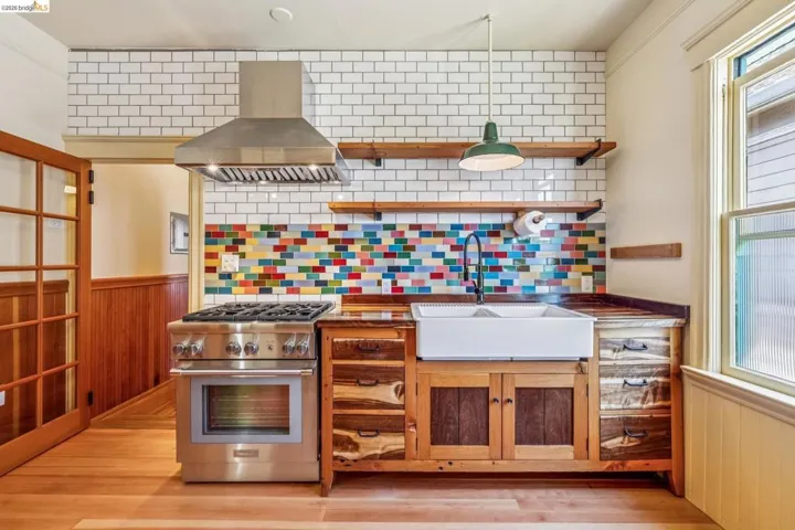 Kitchen featuring island exhaust hood, wood walls, high end range, a wainscoted wall, and tasteful backsplash