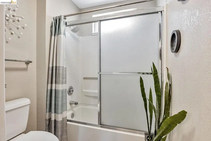 full bathroom with a textured wall and bath / shower combo with glass door