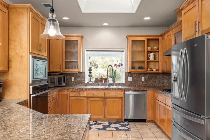 Inside, the open floor plan offers spacious living with abundant natural light and expansive windows that frame the surrounding views. The living room features a cozy gas fireplace and ample space for gathering and entertaining. The kitchen is designed for both function and style, complete with granite countertops, stainless steel appliances, generous counter space, and bar seating, all enhanced by a skylight that fills the space with natural light.