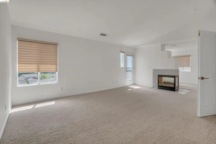 Unfurnished living room with vaulted ceiling, a tile fireplace, and light colored carpet