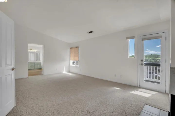 Empty room with light colored carpet, healthy amount of natural light, and vaulted ceiling
