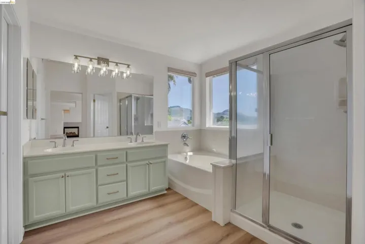 Bathroom featuring double vanity, a shower stall, light wood finished floors, and a garden tub