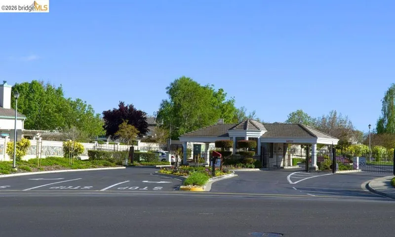 View of asphalt road featuring curbs, a gated entry, and street lights