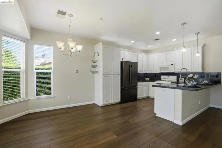 Kitchen with dark countertops, a peninsula, white cabinets, white appliances, and hanging lights