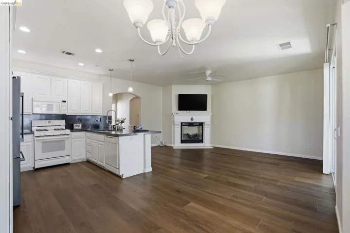 Kitchen featuring a peninsula, dark countertops, white appliances, arched walkways, and white cabinets