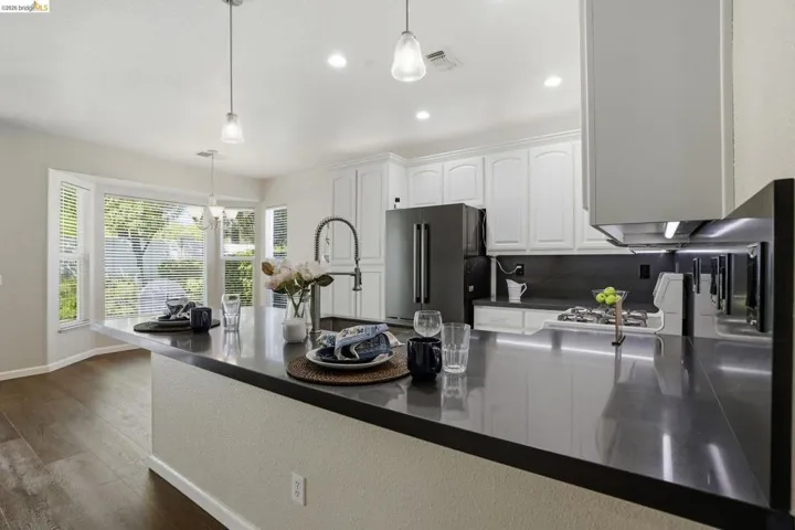 Kitchen with white cabinets, freestanding refrigerator, gas range oven, hanging light fixtures, and dark wood-style flooring