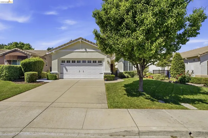 View of front facade with a front yard, driveway, an attached garage, stucco siding, and a tile roof