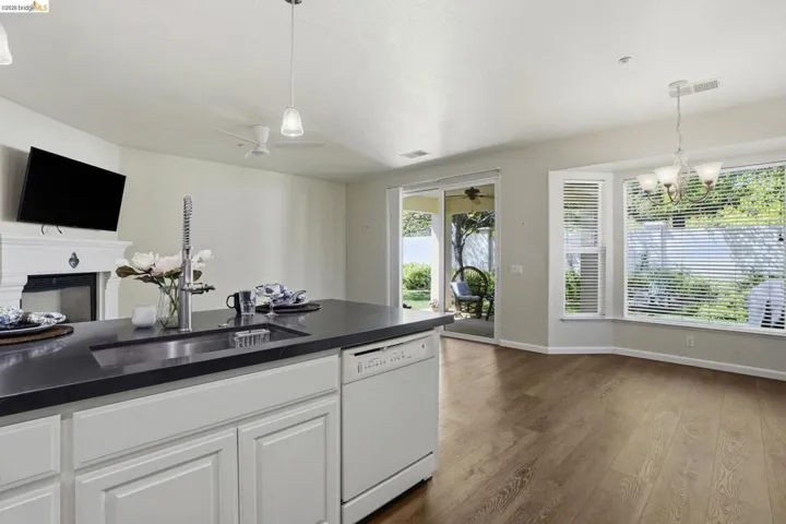 Kitchen with dishwasher, a fireplace, white cabinets, dark wood-type flooring, and a chandelier