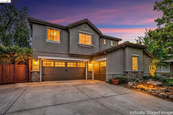 Traditional-style home with stone siding, a garage, stucco siding, concrete driveway, and a gate