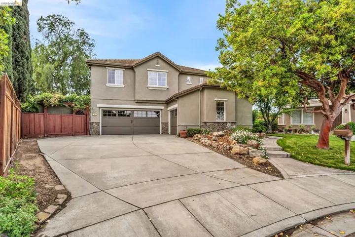 Traditional home with stone siding, stucco siding, a garage, driveway, and a gate