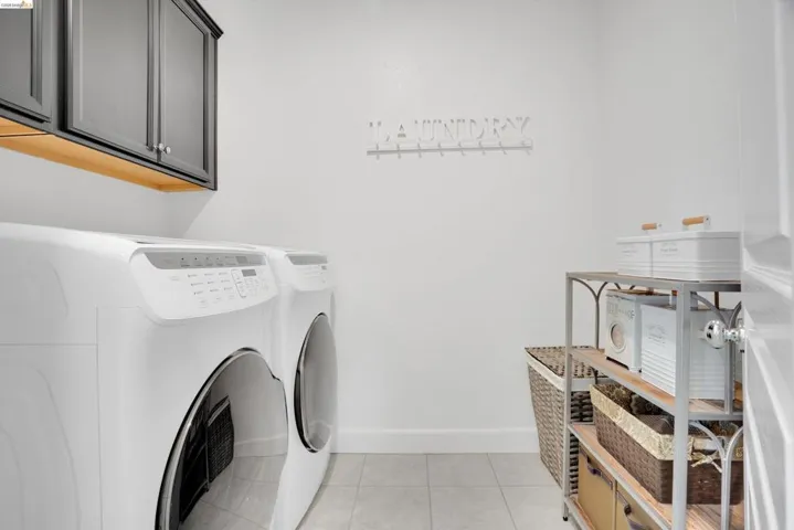 Laundry room featuring washing machine and dryer, light tile patterned floors, and cabinet space