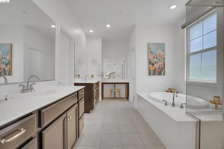 Full bath featuring two vanities, a garden tub, light tile patterned floors, and recessed lighting