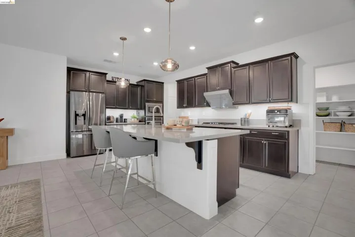 Kitchen with dark wood finish cabinetry, a kitchen breakfast bar, stainless steel appliances, a kitchen island with sink, and light tile patterned floors