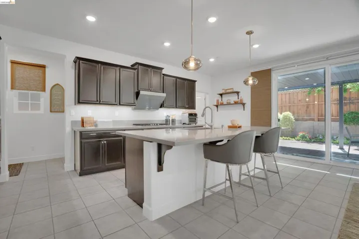 Kitchen with dark wood finish cabinets, a kitchen breakfast bar, a center island with sink, hanging light fixtures, and light tile patterned flooring