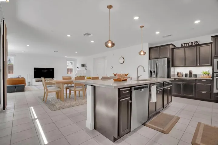 Kitchen featuring dark wood finish cabinetry, stainless steel appliances, open floor plan, and a kitchen island with sink