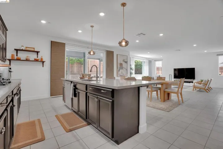 Kitchen featuring dark wood finish cabinetry, hanging light fixtures, a kitchen island with sink, open floor plan, and plenty of natural light