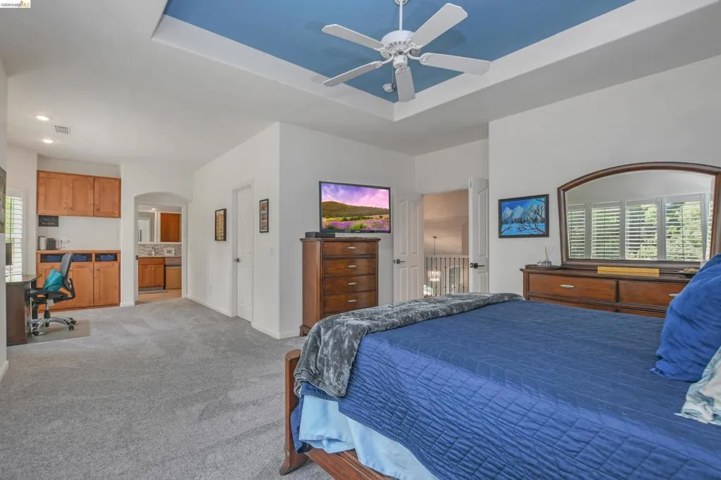 Bedroom with carpet, a desk, ceiling fan, a tray ceiling, and arched walkways
