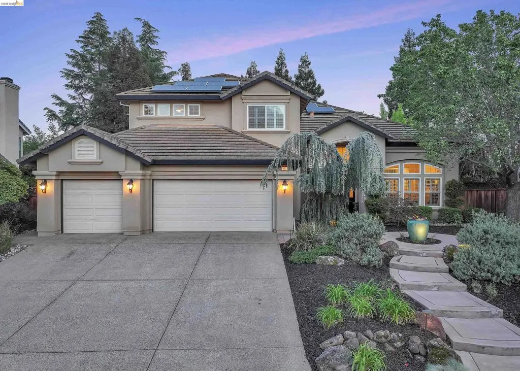 Two-story stucco residence featuring a tile roof, solar panels, and an arched window