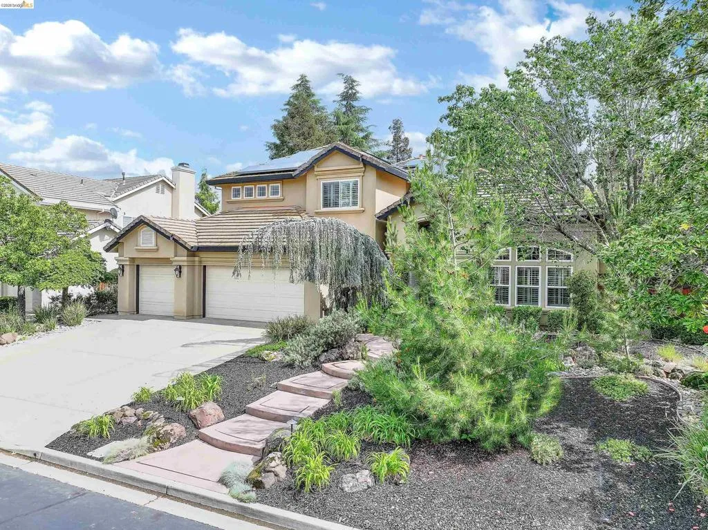 View of front of property with concrete driveway, stucco siding, solar panels, a tile roof, and a chimney