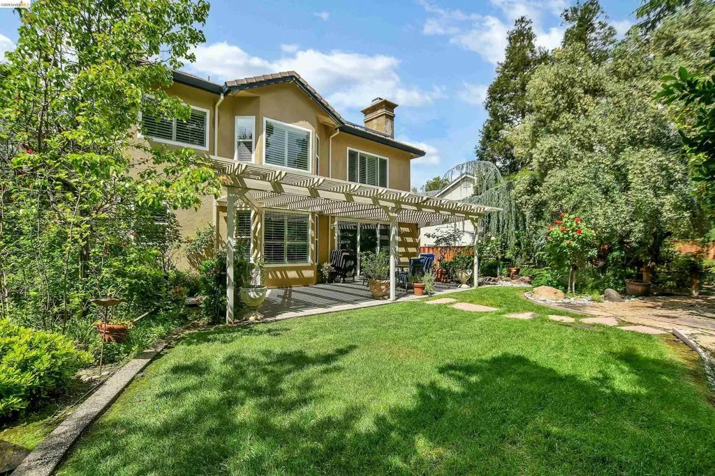 Rear view of house with a pergola, a lawn, stucco siding, and a chimney