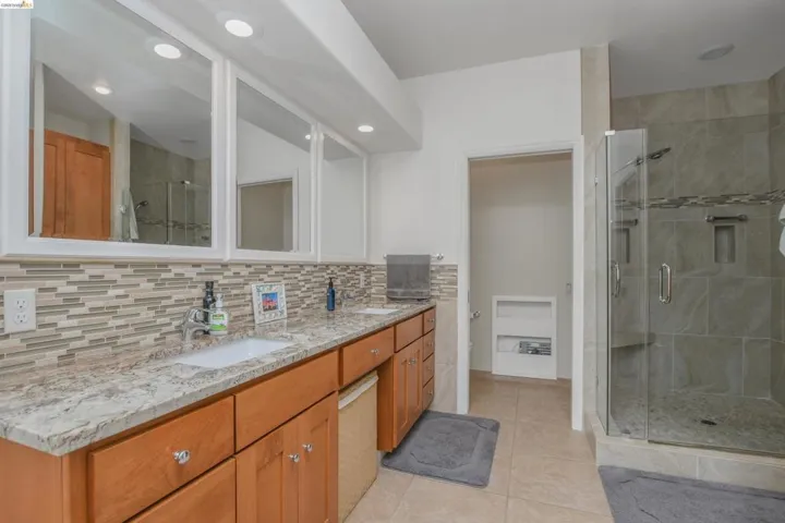 Full bathroom with double vanity, a stall shower, and light tile patterned flooring