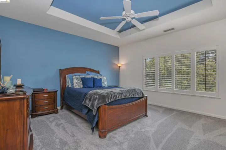 Primary Bedroom featuring a recessed ceiling, carpet flooring, ceiling fan and retreat area.