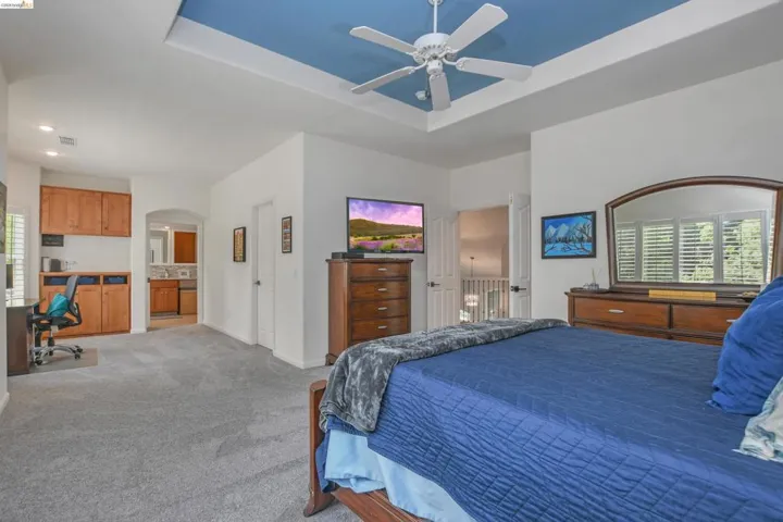 Bedroom with carpet, a desk, ceiling fan, a tray ceiling, and arched walkways