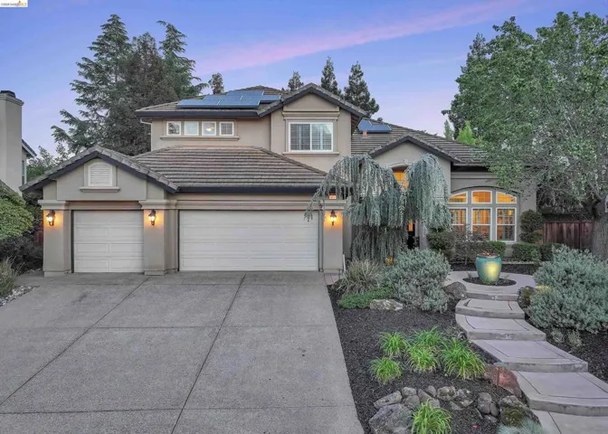 Two-story stucco residence featuring a tile roof, solar panels, and an arched window