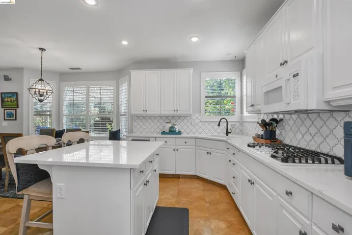 Kitchen with a breakfast bar area, white cabinets, light stone countertops, white appliances, and a kitchen island