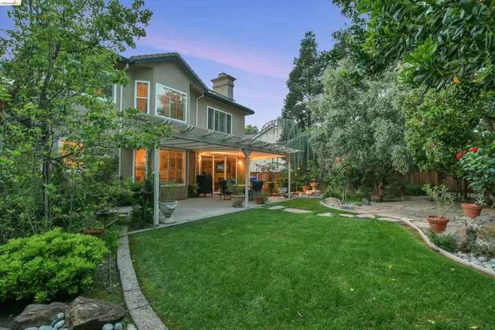 Rear view of house featuring a patio area, stucco siding, a fenced backyard, a chimney, and a pergola