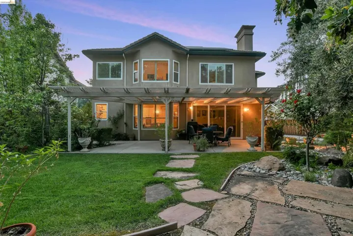 Back of property at dusk with a patio, a pergola, a lawn, and stucco siding