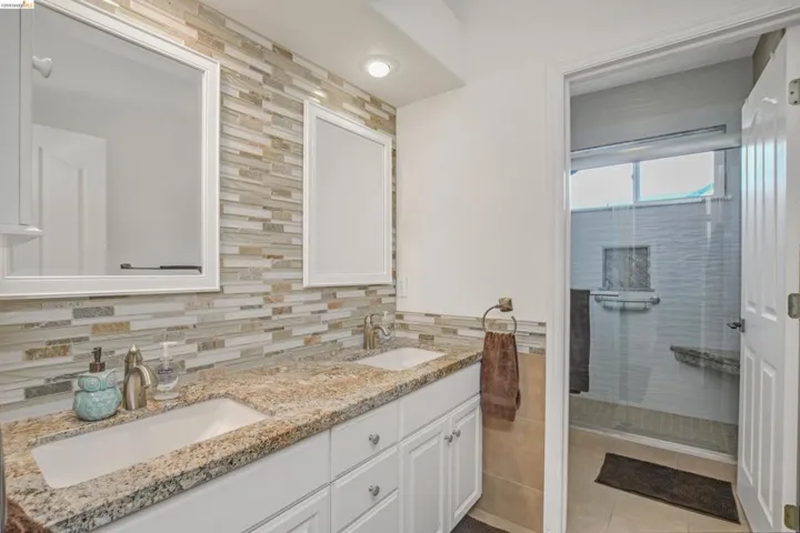 Bathroom with double vanity, a shower stall, and tile walls