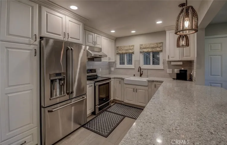 Kitchen showing custom lighting, electric range/cooktop with built in fan for "high heat" cooking, country sink, upgraded cabinetry, and vinyl flooring