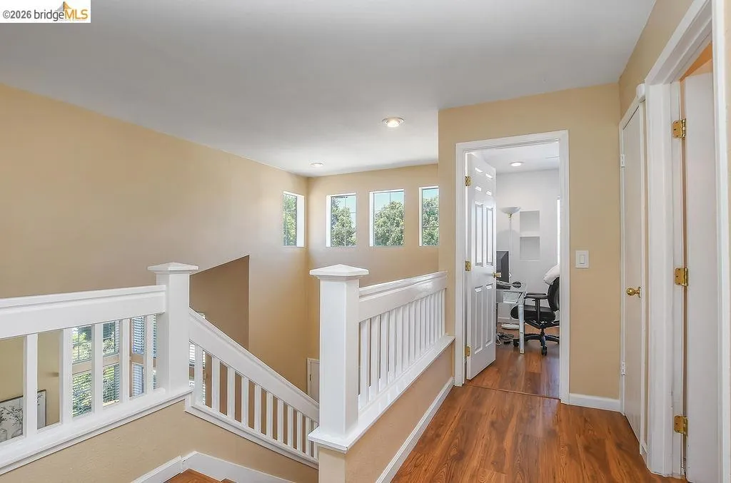 Upper landing with wood-finish flooring, white spindle railings, recessed lighting, and a series of three transom windows