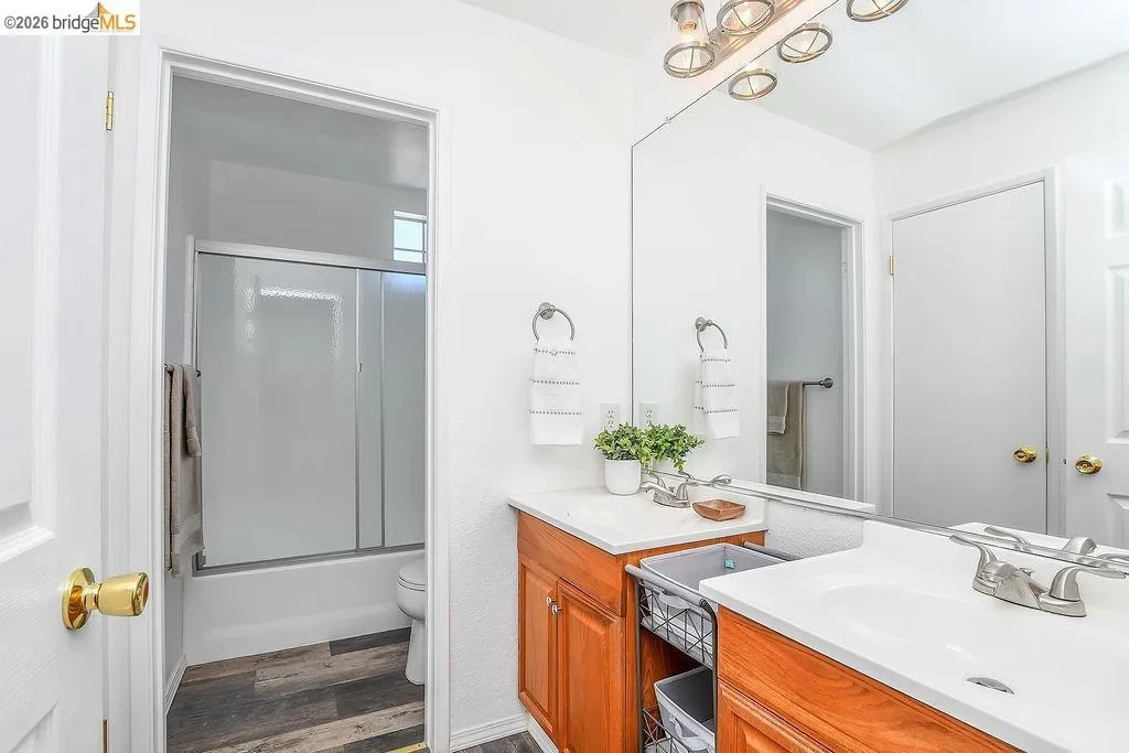 Bathroom featuring a wood-finish vanity with a white countertop and integrated sink, a large wall-mounted mirror, and a tub/shower combination with sliding glass doors