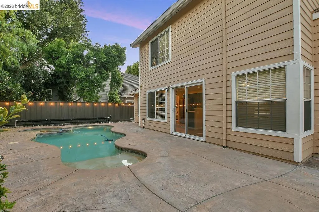 Freeform swimming pool complemented by stamped concrete patio, horizontal siding, and a privacy fence