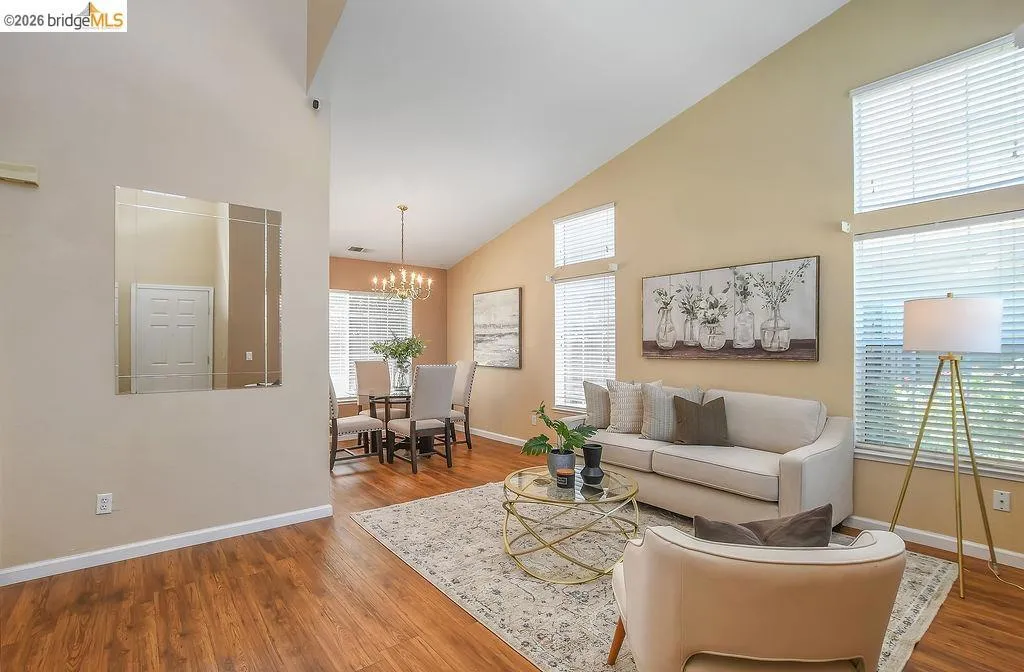 Vaulted ceilings elevate this open-concept living space, featuring wood-finish flooring and ample natural light from multiple large windows