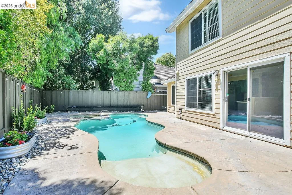 Backyard featuring a freeform swimming pool with integrated spa, concrete decking, and a privacy fence