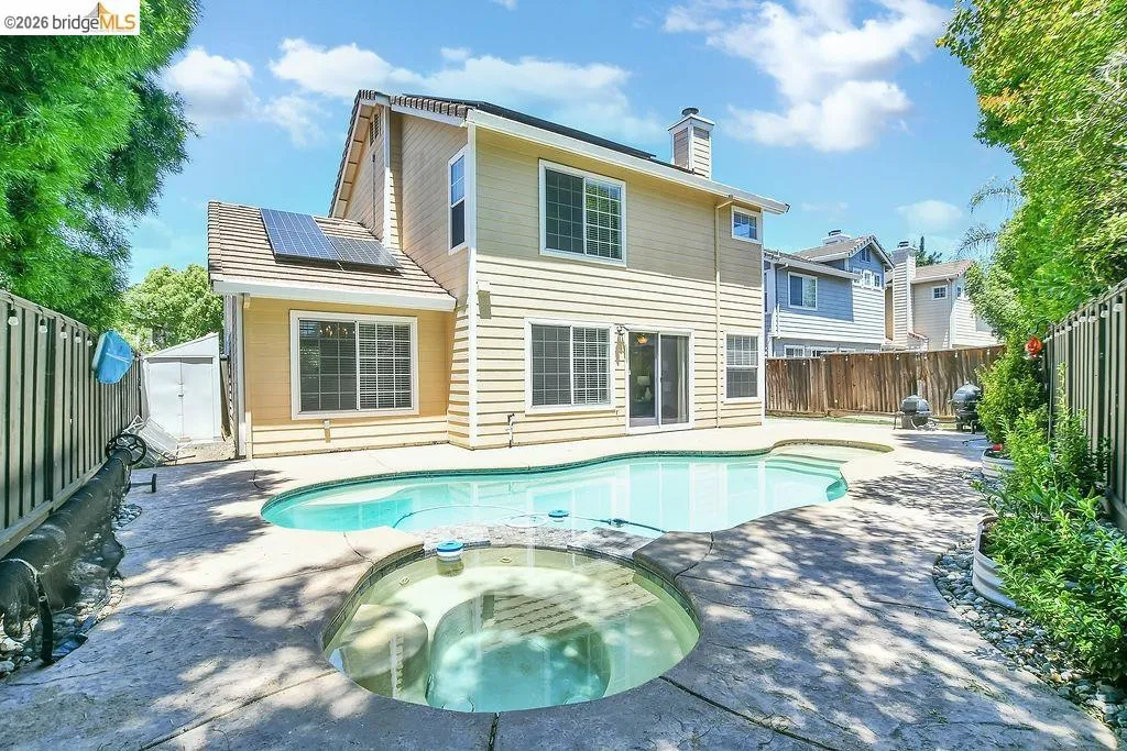 Rear exterior featuring a freeform swimming pool with integrated spa, concrete decking, horizontal siding, multiple windows, and solar panels