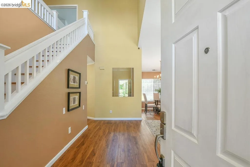 Entryway featuring wood-finish flooring, a white paneled door, and a staircase with white balusters