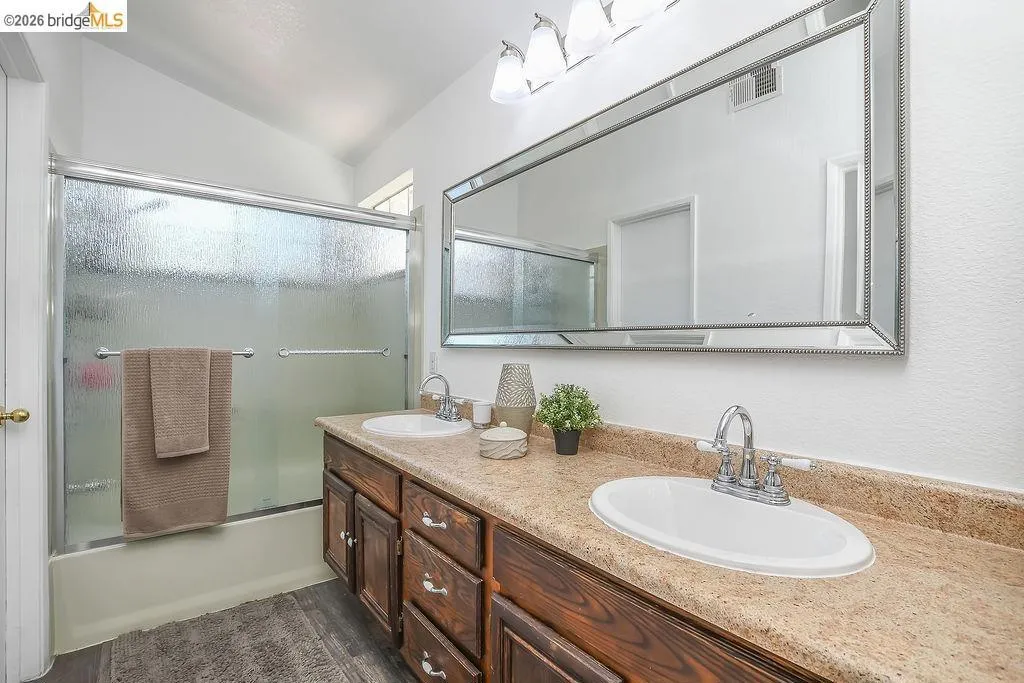 Bathroom featuring a double vanity with wood-finish cabinetry, a large framed mirror, and a shower-over-tub combination with a sliding glass enclosure
