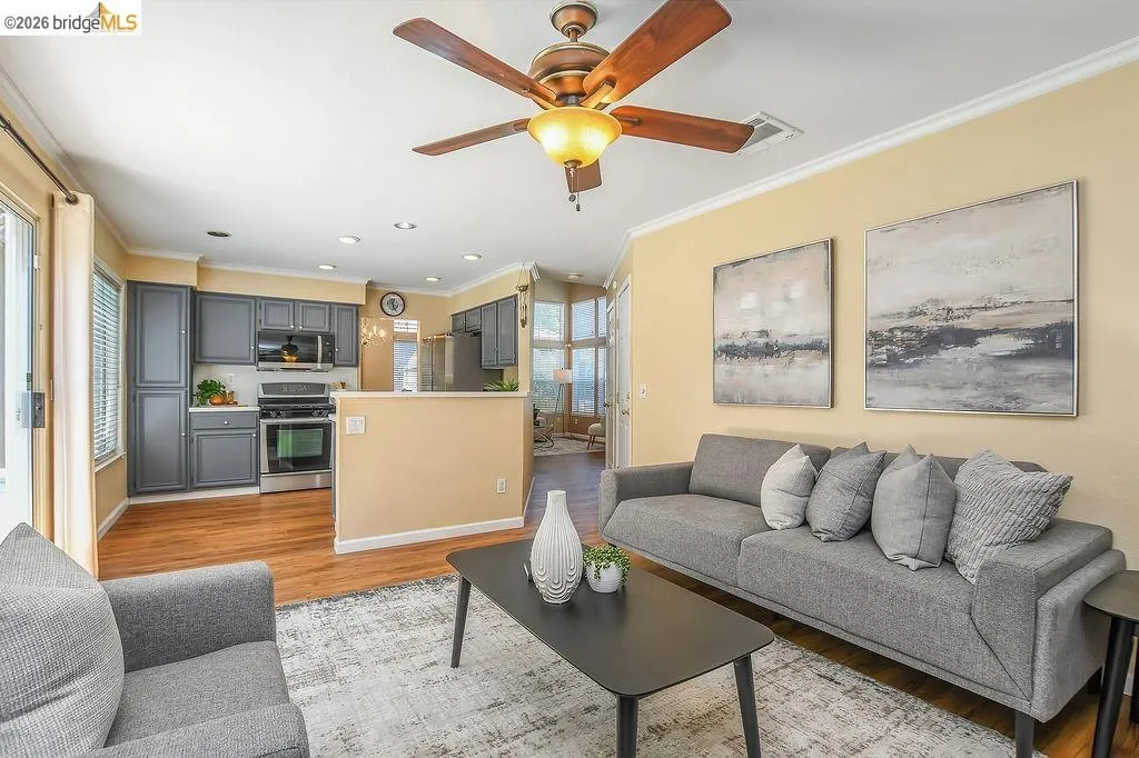 Living room featuring a ceiling fan with integrated lighting, crown molding, and wood-finish flooring